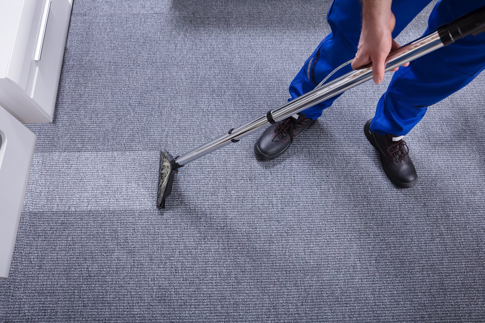 Person vacuuming a carpet with a wand vacuum, top-down view