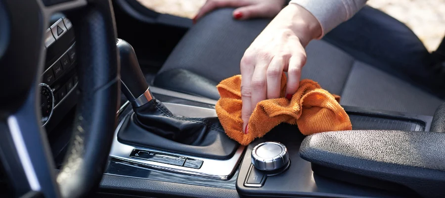 Hand using an orange microfiber cloth to clean a car interior