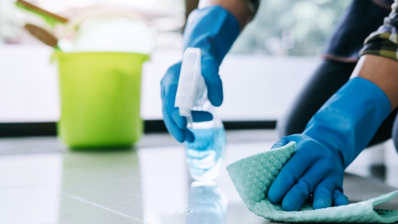 Blue rubber gloves spraying and wiping a tile floor with a green cloth