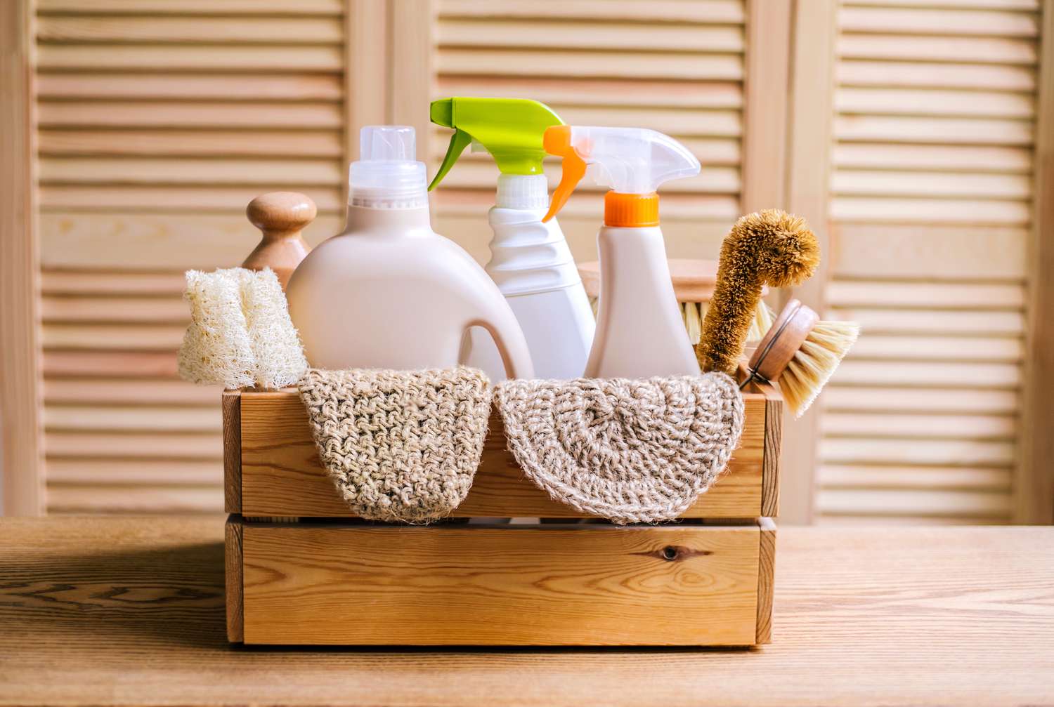 Wooden crate filled with cleaning bottles, brushes, and natural sponges