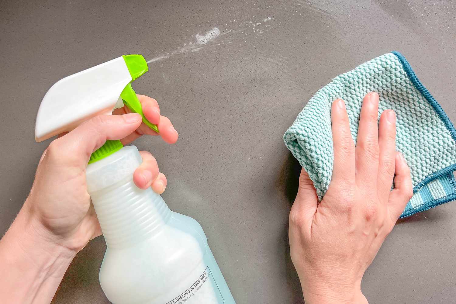 Hands spraying a kitchen counter and wiping with a green microfiber cloth