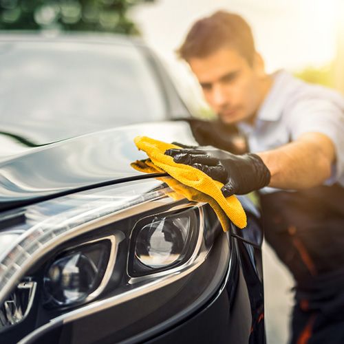 Detailer polishing the front of a black car with a yellow microfiber cloth