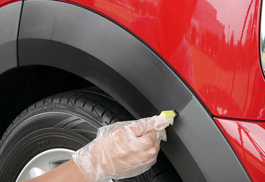 Restoring faded black plastic trim on a red car with a sponge applicator